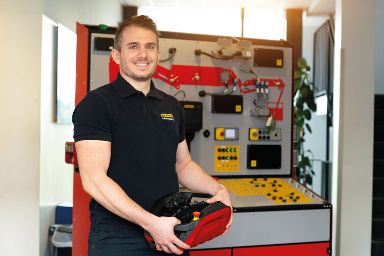 Ein junger Mechatroniker bedient eine PALFINGER Kransteuerung. Im Hintergrund sieht man ein Serviceboard. Ein junger Mechatroniker bedient eine PALFINGER Kransteuerung. Im Hintergrund sieht man ein Serviceboard.