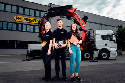 Zwei weibliche und ein männlicher Lehrling stehen vor einem Ladekran vor unserem Standort in Lengau.