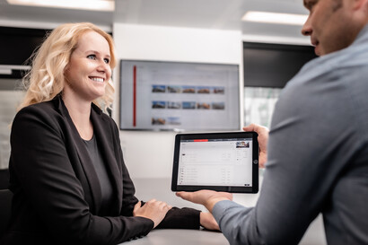 Ein Mitarbeitender aus dem Vertrieb zeigt einer Kundin mögliche Produktkonfigurationen am Tablet.