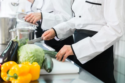 Zwei Personen kochen. Auf der Arbeitsplatte liegt Gemüse.