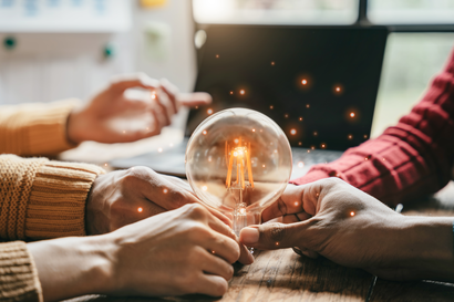 Several hands hold a light bulb that is lit.