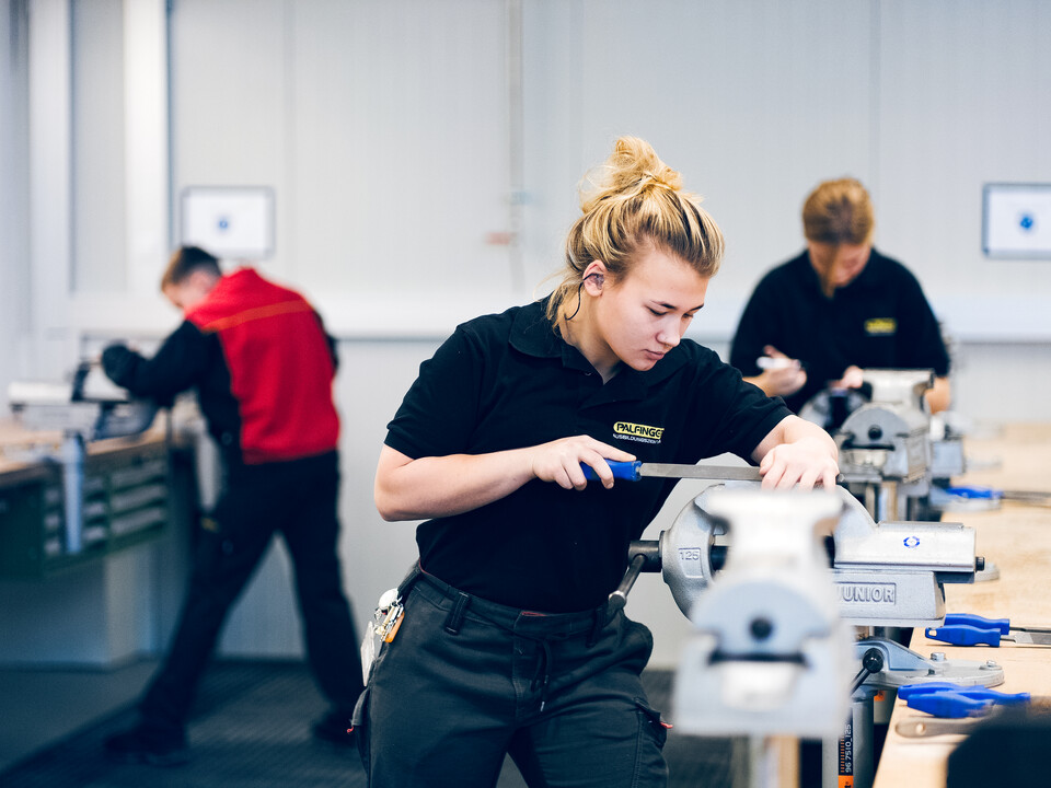Zwei männliche und eine weibliche Auszubildende arbeiten in der Lehrwerkstatt. Zwei männliche und eine weibliche Auszubildende arbeiten in der Lehrwerkstatt.