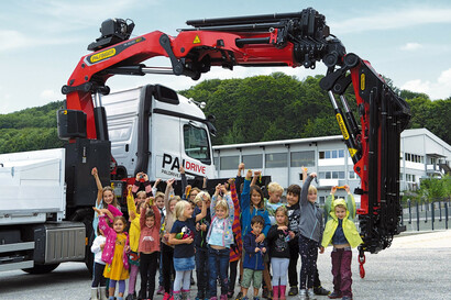 Eine Gruppe von Kindern und Betreuungspersonen stehen vor einem LKW mit PALFINGER Ladekran.